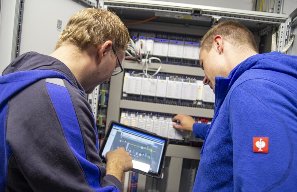 Zwei Mitarbeiter von Kliwa stehen vor einem technischen Gerät und bedienen ein Tablet.